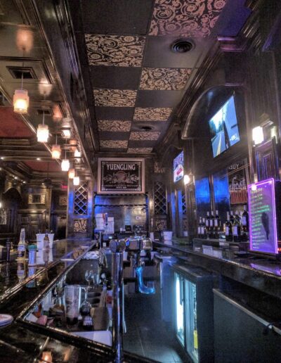 Dimly-lit bar interior with ornate ceiling and stools lined up along the counter.