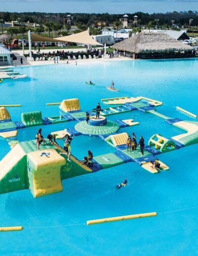 An aerial view of people enjoying a large inflatable obstacle course on a clear blue lake.