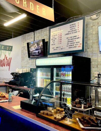 A modern cafe counter with menu boards, a display of baked goods, and a refrigerated section for cold beverages.