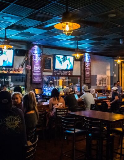 Patrons socializing at a dimly lit bar with televisions and daily specials advertised.