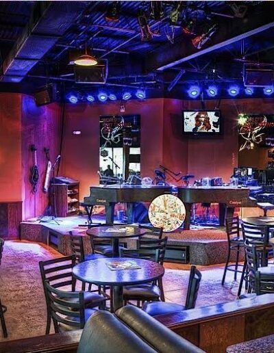 An empty, dimly-lit bar with televisions, a stage for live music, and scattered seating.