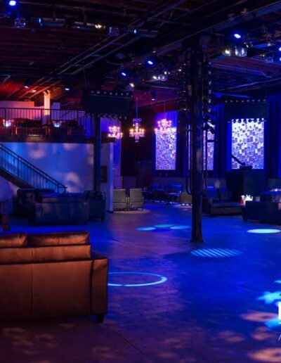 A spacious event venue with comfortable seating, blue ambient lighting, and a text overlay "district 3 arts & events.