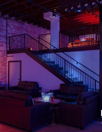 Modern event space with ambient blue lighting, comfortable seating, and exposed brick walls.