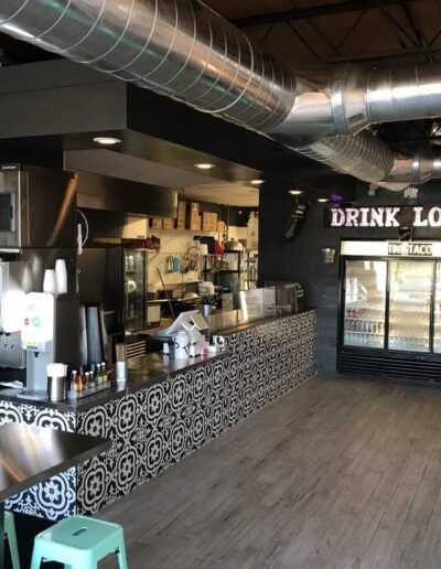 Interior of a modern cafe with a counter, "drink local" sign, and seating area.